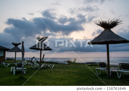 Thatched-roof parasols and beach beds line the coast at dawn on the French island of Corsica in the Mediterranean Sea. Thatched-roof parasols and beach beds line the coast at dawn on the French island of Corsica in the Mediterranean Sea. 138761646