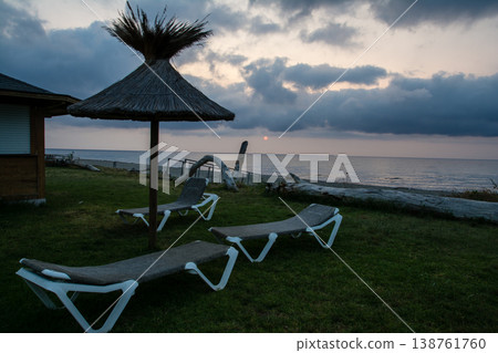 在地中海的法國科西嘉島,黎明時分,茅草屋頂的遮陽傘和沙灘床沿著海岸線排列。 在地中海的法國科西嘉島,黎明時分,茅草屋頂的遮陽傘和沙灘床沿著海岸線排列。 138761760
