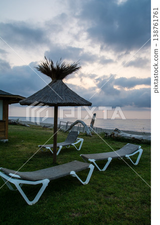 Thatched-roof parasols and beach beds line the coast at dawn on the French island of Corsica in the Mediterranean Sea. Thatched-roof parasols and beach beds line the coast at dawn on the French island of Corsica in the Mediterranean Sea. 138761761
