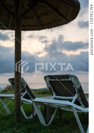 在地中海的法國科西嘉島,黎明時分,茅草屋頂的遮陽傘和沙灘床沿著海岸線排列。 在地中海的法國科西嘉島,黎明時分,茅草屋頂的遮陽傘和沙灘床沿著海岸線排列。 138761764