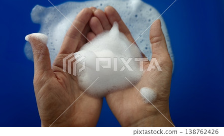 Hands holding soap foam on a blue background while bubbles scatter around 138762426