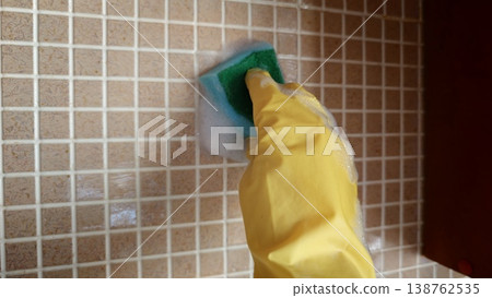 Scrubbing tiles with a sponge covered in soap inside a kitchen Scrubbing tiles with a sponge covered in soap inside a kitchen 138762535