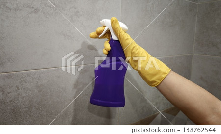 Person holding a purple cleaning spray bottle in a bathroom setting at home Person holding a purple cleaning spray bottle in a bathroom setting at home 138762544