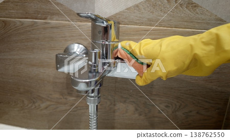 Cleaning a shiny faucet in a bathroom with a sponge and rubber glove Cleaning a shiny faucet in a bathroom with a sponge and rubber glove 138762550