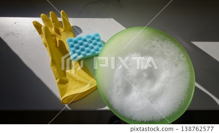 Soap and sponge next to yellow gloves on a table with bubbles in a bowl Soap and sponge next to yellow gloves on a table with bubbles in a bowl 138762577