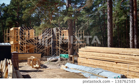 Construction site of wooden building in forest area with lumber stacked nearby Construction site of wooden building in forest area with lumber stacked nearby 138762585