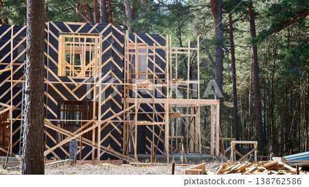Construction of a wooden house in a forested area during daylight hours. frame house Construction of a wooden house in a forested area during daylight hours. frame house 138762586