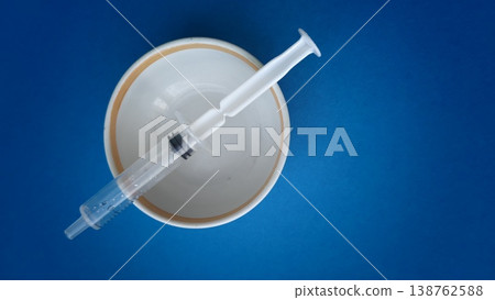 Syringe placed on a white bowl against a blue background during a health activity Syringe placed on a white bowl against a blue background during a health activity 138762588