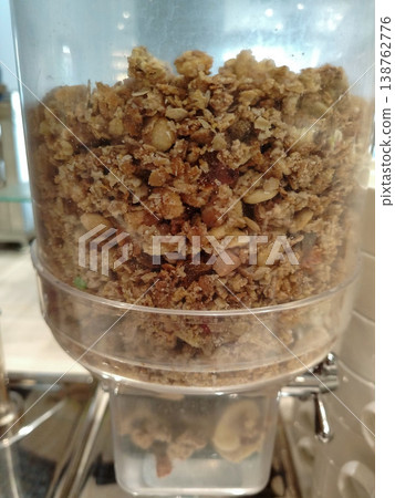 Granola dispenser filled with mixed granola ingredients including oats, nuts, and seeds, positioned in a buffet-style setting for breakfast options 138762776