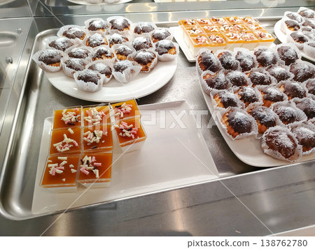 Assorted desserts displayed on a stainless steel tray, featuring chocolate cupcakes with icing and jelly cups topped with coconut and nuts Assorted desserts displayed on a stainless steel tray, featuring chocolate cupcakes with icing and jelly cups topped with coconut and nuts 138762780