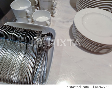 Stainless steel cutlery arranged neatly in a white dish beside white plates and cups on a marble countertop in a modern kitchen setting Stainless steel cutlery arranged neatly in a white dish beside white plates and cups on a marble countertop in a modern kitchen setting 138762782
