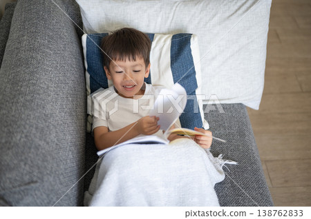 Happy Boy Enjoying a Book at Home on a Cozy Couch with Soft Lighting 138762833