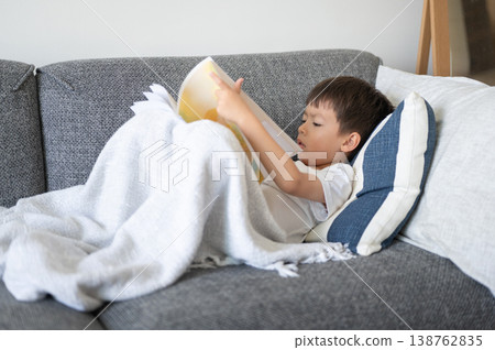 Multiracial Boy Cozy on Sofa Reading a Book Under a Blanket in Bright Home Setting Multiracial Boy Cozy on Sofa Reading a Book Under a Blanket in Bright Home Setting 138762835