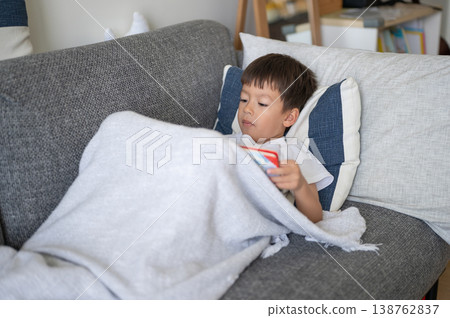 Boy Cozy at Home Reading a Book on a Sofa Under a Blanket 138762837