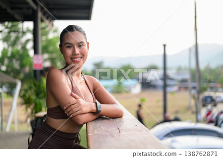 Smiling Thai Fitness Influencer Leaning on Balcony at Sunset Healthy Lifestyle Concept Smiling Thai Fitness Influencer Leaning on Balcony at Sunset Healthy Lifestyle Concept 138762871