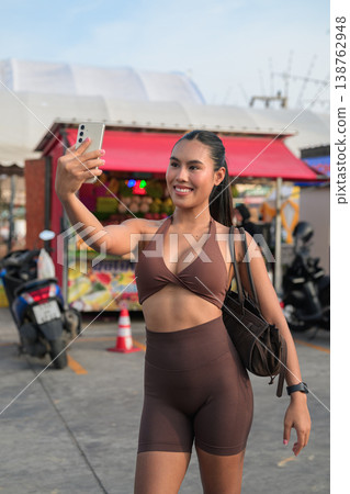 Young Thai Woman Taking Selfie in Brown Activewear at Outdoor Market Modern Digital Lifestyle Concept Young Thai Woman Taking Selfie in Brown Activewear at Outdoor Market Modern Digital Lifestyle Concept 138762948