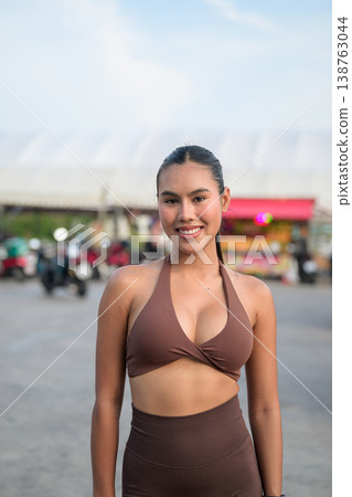 Smiling Young Thai Fitness Influencer in Brown Activewear at Outdoor Market Healthy Lifestyle Concept Smiling Young Thai Fitness Influencer in Brown Activewear at Outdoor Market Healthy Lifestyle Concept 138763044
