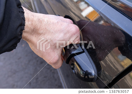 With determination, a man reaches for the handle of a stylish black car, excitement evident as he prepares to embark on his journey 138763057