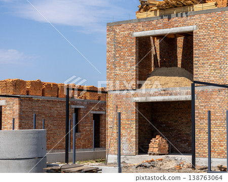 Experienced workers assemble a brick house, with beams of timber stacked high under a clear blue sky, signaling progress and hard work Experienced workers assemble a brick house, with beams of timber stacked high under a clear blue sky, signaling progress and hard work 138763064