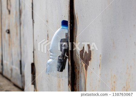 A closed metal garage stands quietly, featuring a plastic bottle and a key hanging from its door, adding an unexpected charm to the scene A closed metal garage stands quietly, featuring a plastic bottle and a key hanging from its door, adding an unexpected charm to the scene 138763067