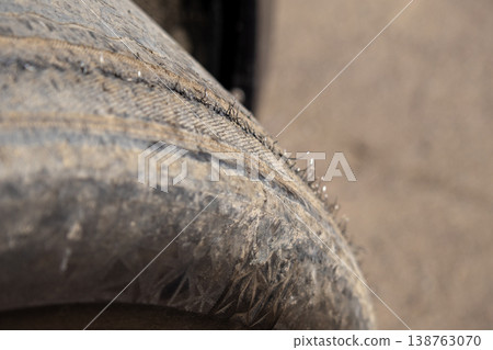 A close-up view of a damaged car tire shows exposed metal cords, highlighting the wear and tear after rough driving on a dusty road A close-up view of a damaged car tire shows exposed metal cords, highlighting the wear and tear after rough driving on a dusty road 138763070