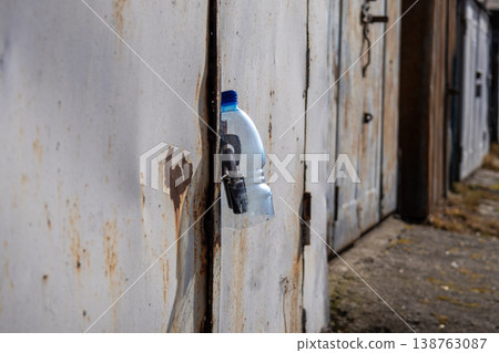Rusty metal garage reveals stories of abandonment, with a water bottle peeking through its weathered door in a quiet urban setting Rusty metal garage reveals stories of abandonment, with a water bottle peeking through its weathered door in a quiet urban setting 138763087