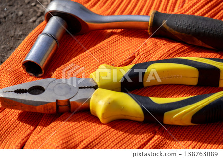 Pliers and a wrench are laid carefully on bright gloves, hinting at a busy workshop where hands create and fix with passion Pliers and a wrench are laid carefully on bright gloves, hinting at a busy workshop where hands create and fix with passion 138763089