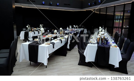 Modern restaurant interior featuring crisp white tablecloths, black chair covers, minimalist flower centerpieces, empty wine glasses, and pristine appetizer plates Modern restaurant interior featuring crisp white tablecloths, black chair covers, minimalist flower centerpieces, empty wine glasses, and pristine appetizer plates 138763261