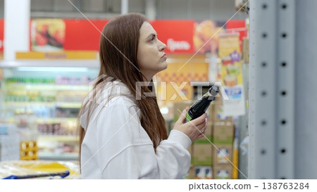 Young woman carefully selecting soy sauce at a supermarket, making informed choices about food products by reading the label on the bottle Young woman carefully selecting soy sauce at a supermarket, making informed choices about food products by reading the label on the bottle 138763284