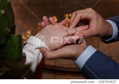 Groom placing diamond engagement ring on bride finger during wedding ceremony with bokeh background Groom placing diamond engagement ring on bride finger during wedding ceremony with bokeh background 138763427