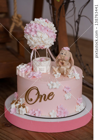 Pink First Birthday Cake with Cute Bunny and Hot Air Balloon Topper on Wooden Surface Pink First Birthday Cake with Cute Bunny and Hot Air Balloon Topper on Wooden Surface 138763441