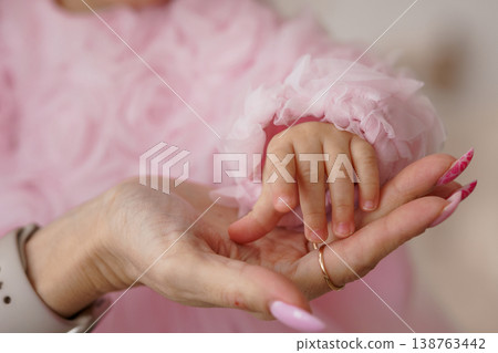 Close-up of mother holding baby hand with pink manicure and soft ruffled sleeve in tender family portrait 138763442