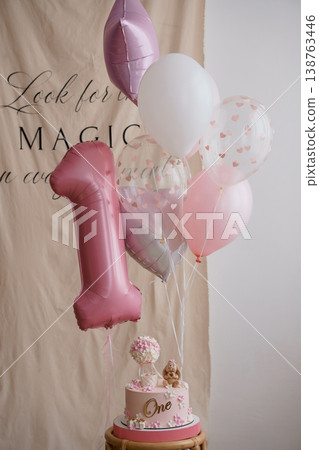 Elegant pink first birthday cake with number one balloon and floral decorations on wooden stand against neutral backdrop. Elegant pink first birthday cake with number one balloon and floral decorations on wooden stand against neutral backdrop. 138763446