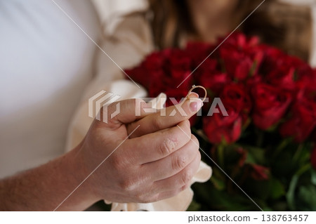 Person Holding Gold Diamond Engagement Ring Near Red Rose Bouquet in Soft Romantic Lighting 138763457