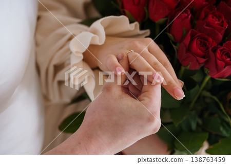 Close-up of man placing engagement ring on woman finger with red roses in background, romantic wedding proposal moment. Close-up of man placing engagement ring on woman finger with red roses in background, romantic wedding proposal moment. 138763459