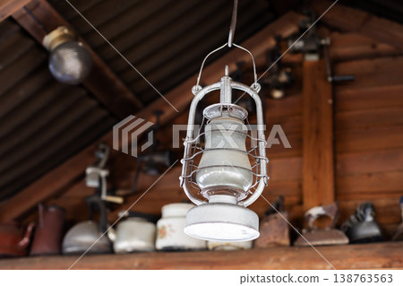 Antique enamel lighting casts gentle warmth over wooden beams with dust particles flickering gently Antique enamel lighting casts gentle warmth over wooden beams with dust particles flickering gently 138763563