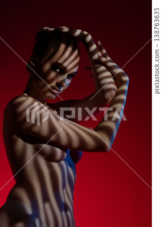 Woman poses gracefully against a red background with striking shadows at night Woman poses gracefully against a red background with striking shadows at night 138763635