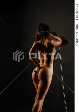 Woman washing herself under the shower, holding shower head Woman washing herself under the shower, holding shower head 138763671