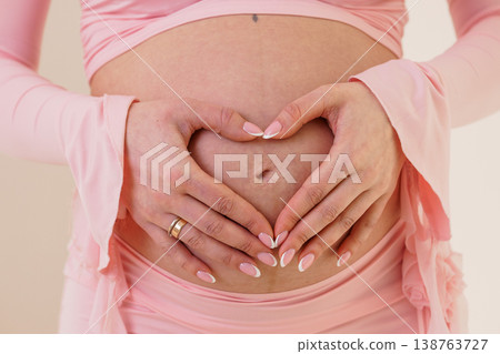 Pregnant Woman Making Heart Shape With Hands Over Her Belly in Pink Clothing Pregnant Woman Making Heart Shape With Hands Over Her Belly in Pink Clothing 138763727