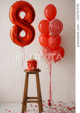 Birthday party celebration setup with red balloons and cake on wooden stool against white background 138763748