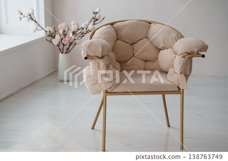 Modern beige plush armchair with gold frame in minimalist white interior with spring flowers Modern beige plush armchair with gold frame in minimalist white interior with spring flowers 138763749