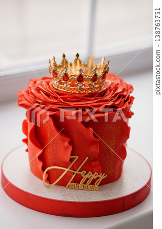Red ruffled birthday cake topped with gold jeweled crown on white surface with glitter and script plaque 138763751