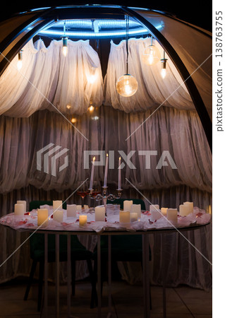 Romantic candlelit dinner setup inside a luxury glamping tent with white fabric drapes and warm ambient lighting 138763755