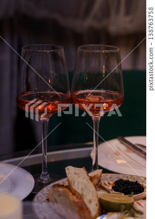 Two glasses of pink wine with caviar and bread on a dark dining table at a luxury restaurant event. Two glasses of pink wine with caviar and bread on a dark dining table at a luxury restaurant event. 138763758