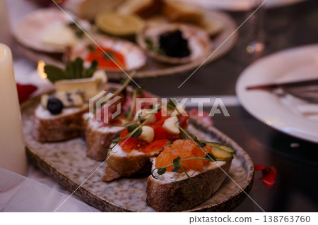 Gourmet salmon and cheese bruschetta on rustic ceramic platter with candles and blurred background. Gourmet salmon and cheese bruschetta on rustic ceramic platter with candles and blurred background. 138763760