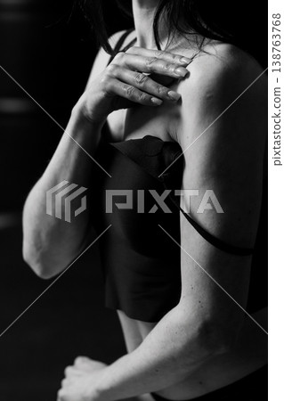 Black and white portrait of woman touching shoulder in black top with dramatic lighting Black and white portrait of woman touching shoulder in black top with dramatic lighting 138763768