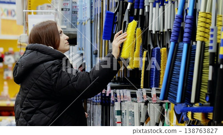 Customer selecting a snow brush from a wide assortment in the automotive department of a supermarket, preparing for winter weather and car care Customer selecting a snow brush from a wide assortment in the automotive department of a supermarket, preparing for winter weather and car care 138763827