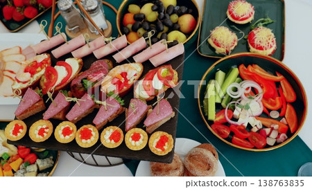 Gourmet buffet display featuring colorful appetizers, bruschetta, fresh produce, and pastries arranged for elegant catered gathering Gourmet buffet display featuring colorful appetizers, bruschetta, fresh produce, and pastries arranged for elegant catered gathering 138763835