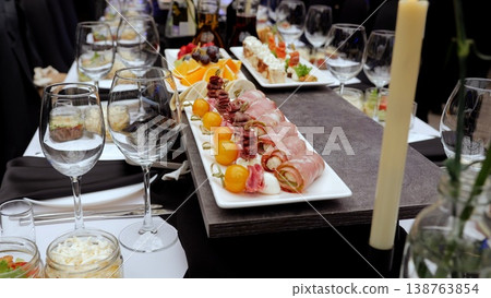 Elegant canapes arranged on white rectangular plate, surrounded by wine glasses, fruits, and candlelight, creating sophisticated dining atmosphere Elegant canapes arranged on white rectangular plate, surrounded by wine glasses, fruits, and candlelight, creating sophisticated dining atmosphere 138763854