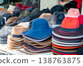 Fashion Stylist Picks Colorful Layered Hats Amidst Lively Outdoor Marketplace Setting 138763875